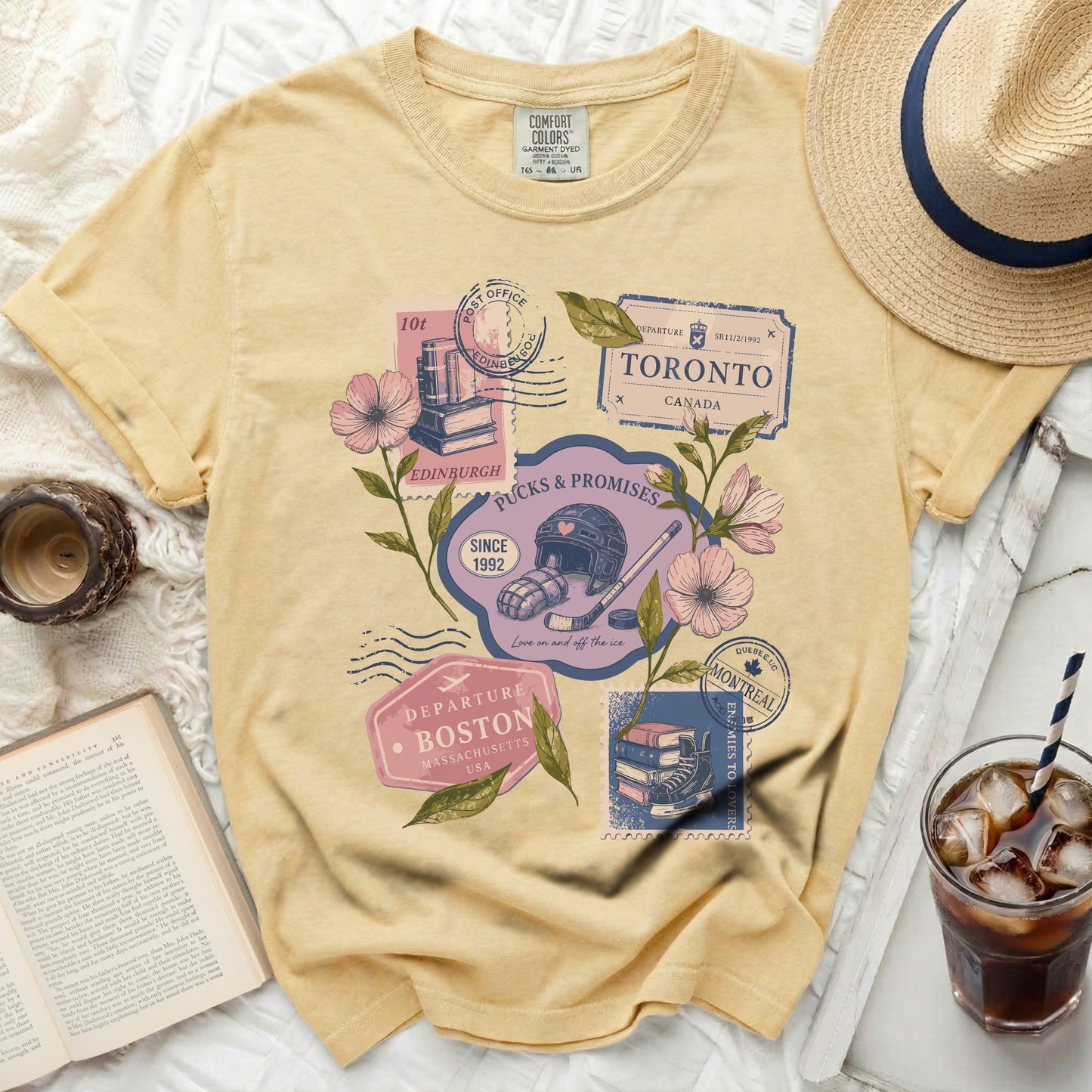 Yellow t-shirt with graphic of travel stamps, hockey gear, and flowers.