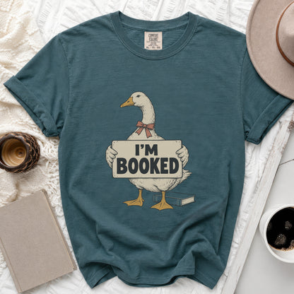 Goose wearing a bow tie holds a sign that says "I'M BOOKED" with a book nearby.