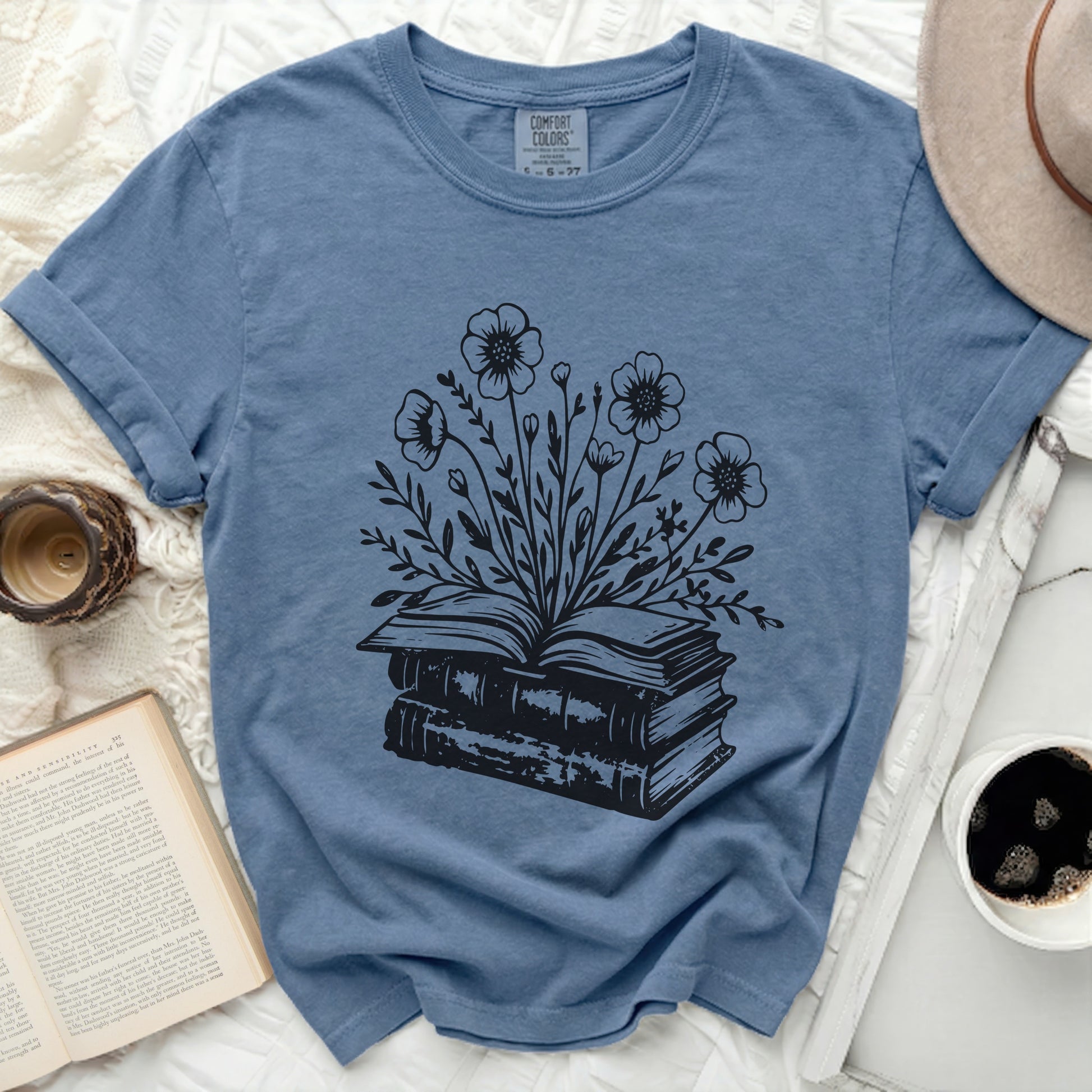 Blue t-shirt with black illustration of an open book with flowers growing from it.