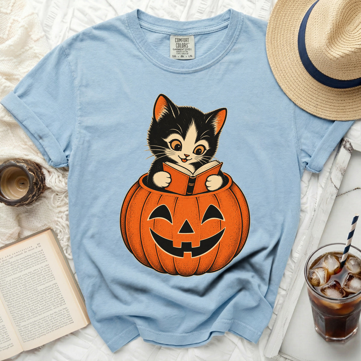 Light blue t-shirt with black and orange cat sitting in a pumpkin and reading.