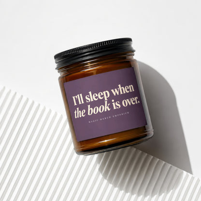 Amber jar candle with purple label reading "I'll sleep when the book is over."