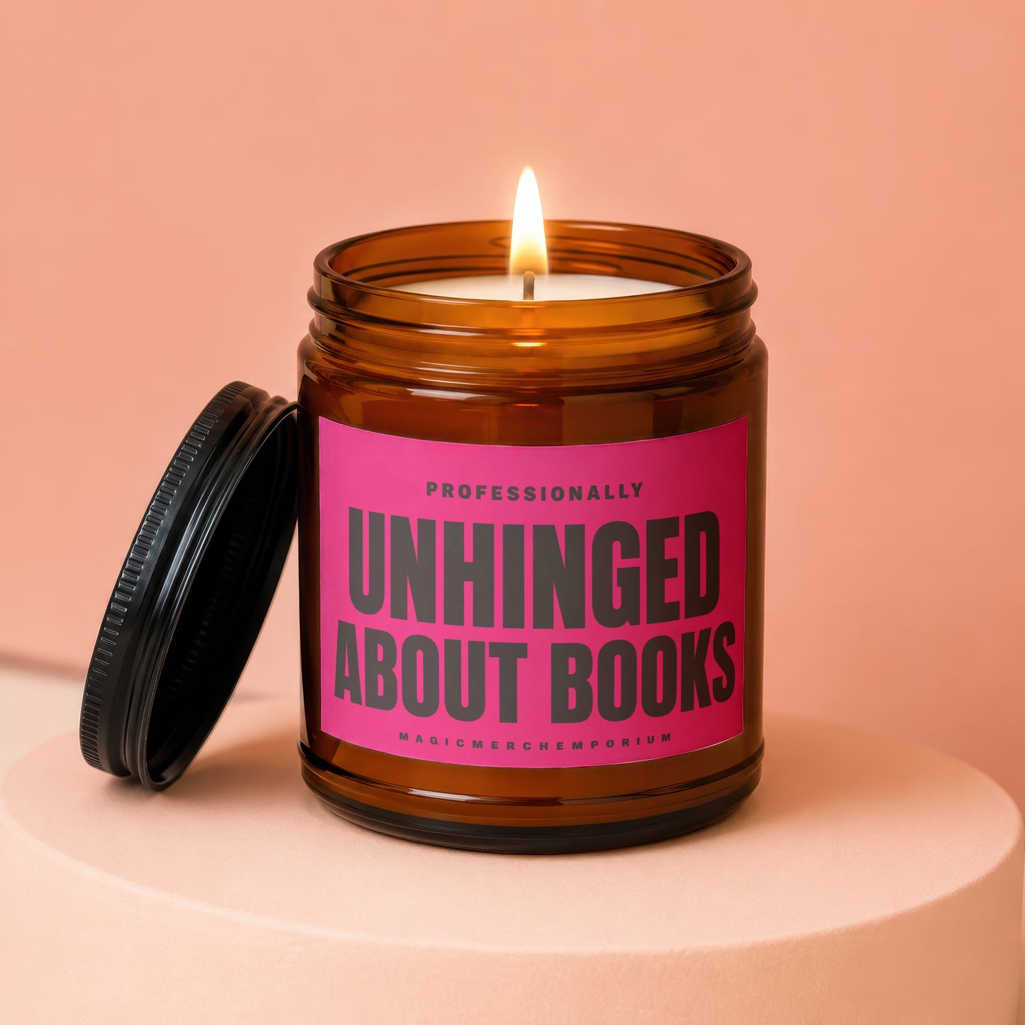 Amber jar candle with lit wick and pink label reading "Professionally Unhinged About Books."