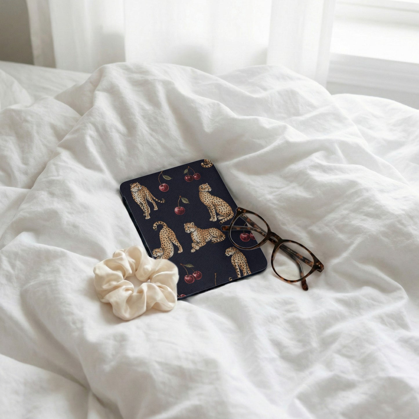 Dark journal with leopard and cherry print, scrunchie, and glasses on white linens.