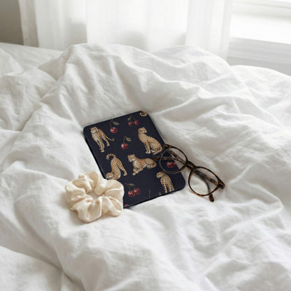 Dark journal with leopard and cherry print, scrunchie, and glasses on white linens.