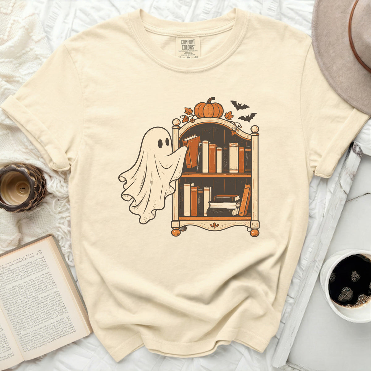 Ghost reaching for book on shelf with pumpkin and bats, on a cream t-shirt.