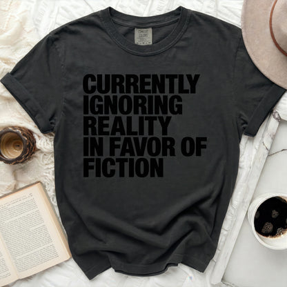 Black t-shirt with "Currently Ignoring Reality In Favor Of Fiction" text.