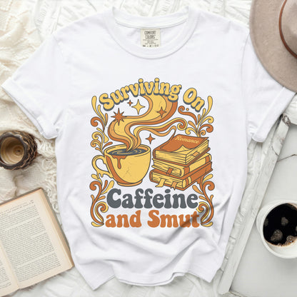 White t-shirt with "Surviving On Caffeine and Smut" graphic.