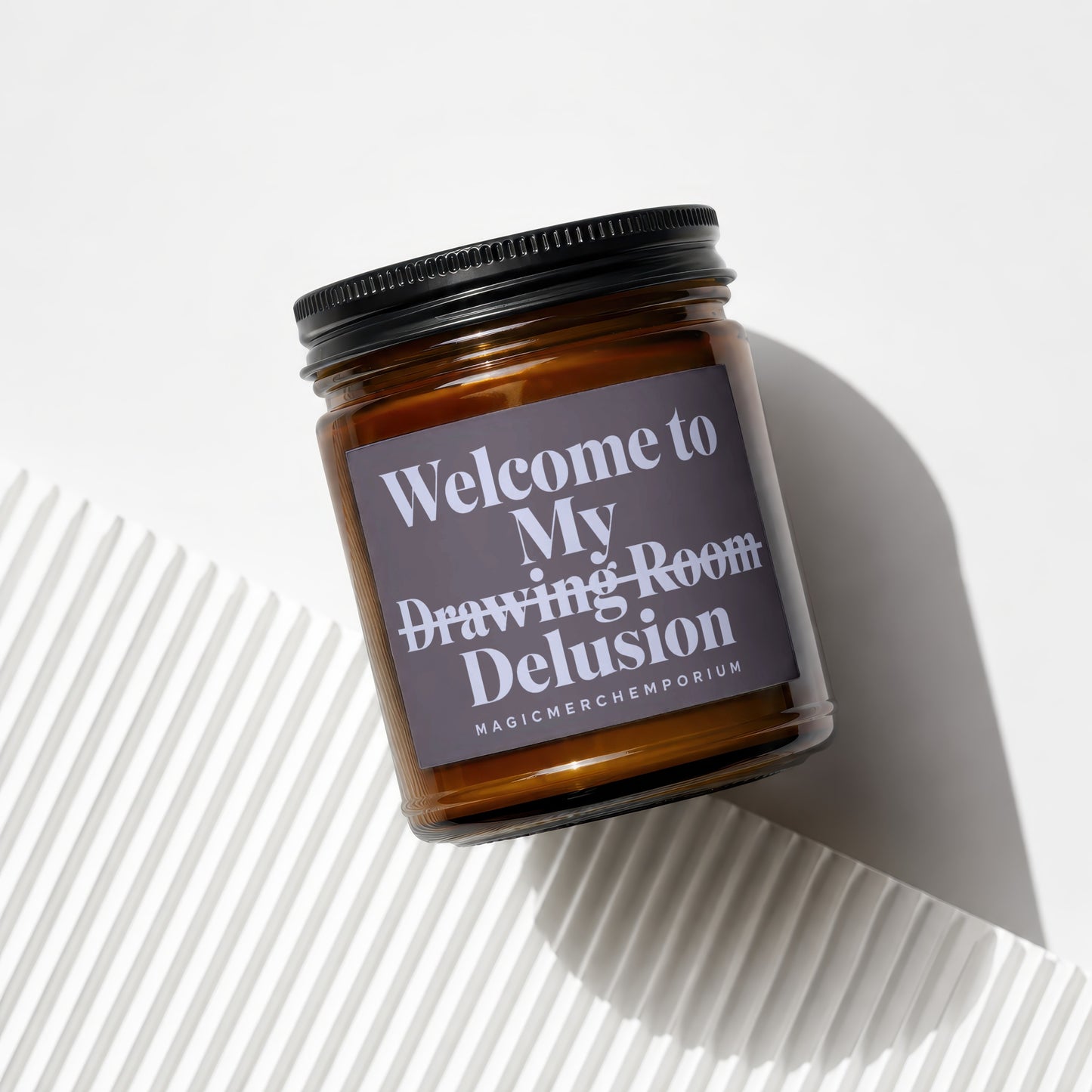 Amber jar candle with black lid labeled "Welcome to My Drawing Room Delusion".