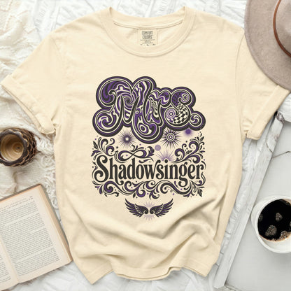 Cream t-shirt with "Shadowsinger" in purple stylized lettering and decorative elements.
