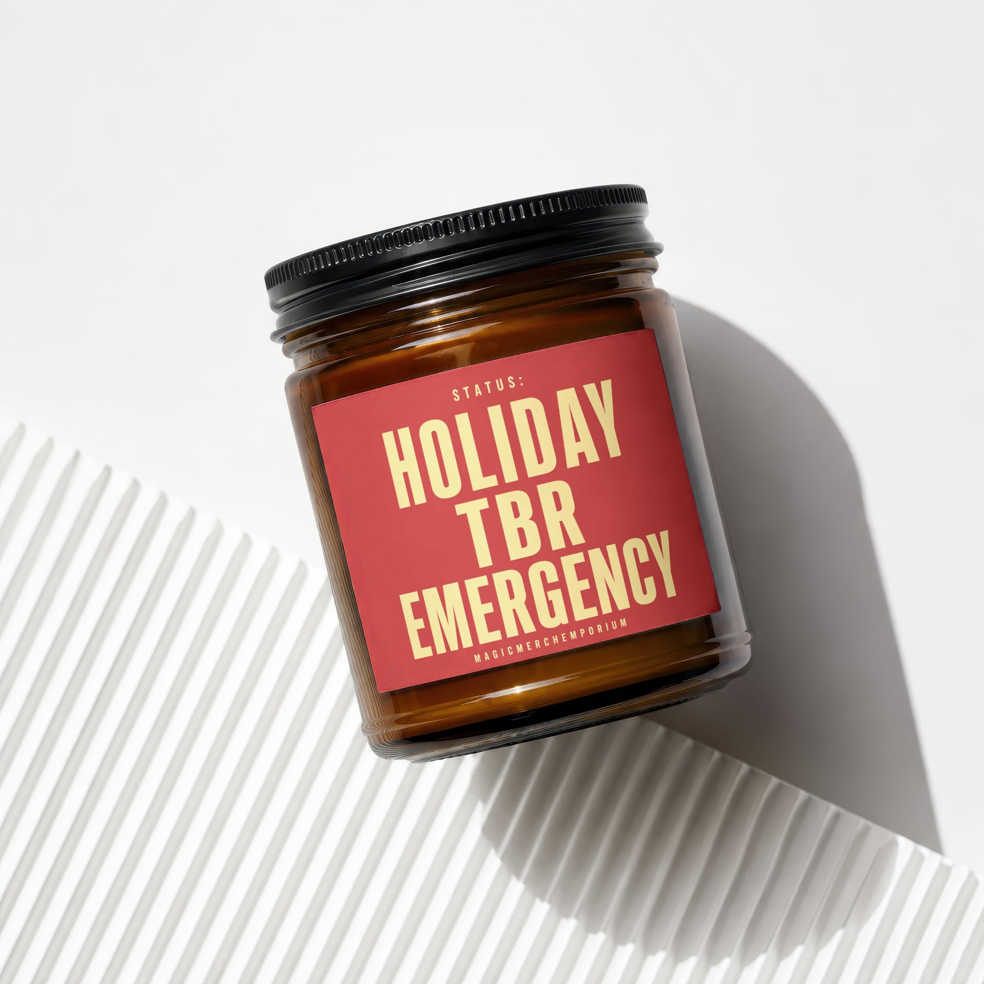 Amber candle in glass jar with red label reading "Status: Holiday TBR Emergency"