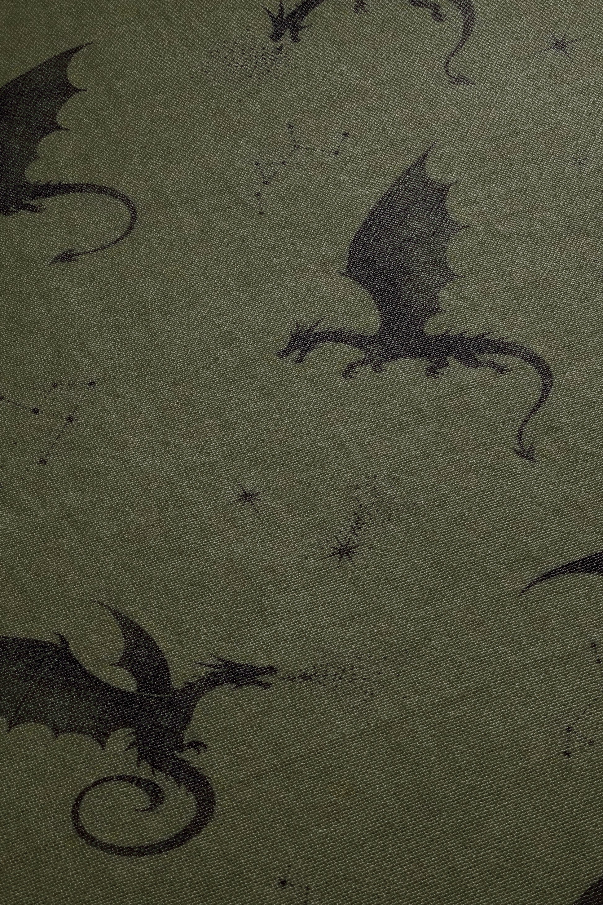 a close-up view of a dark green fabric with a repeating pattern of black silhouettes of dragons.