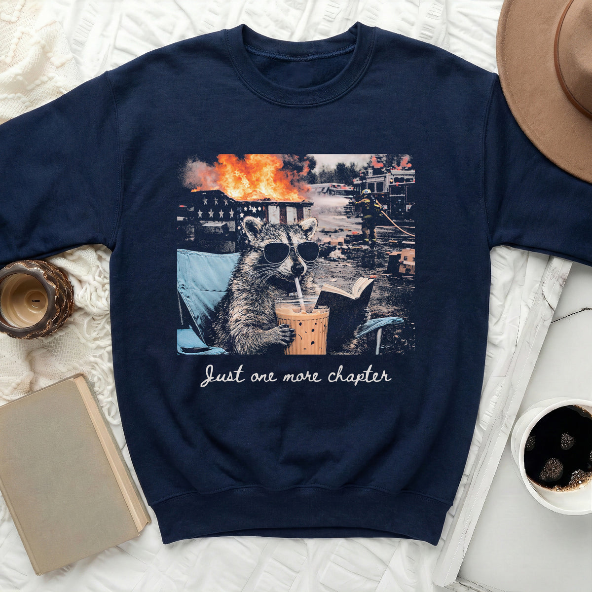 Navy sweatshirt with raccoon wearing sunglasses drinking iced coffee and "Just one more chapter" text.