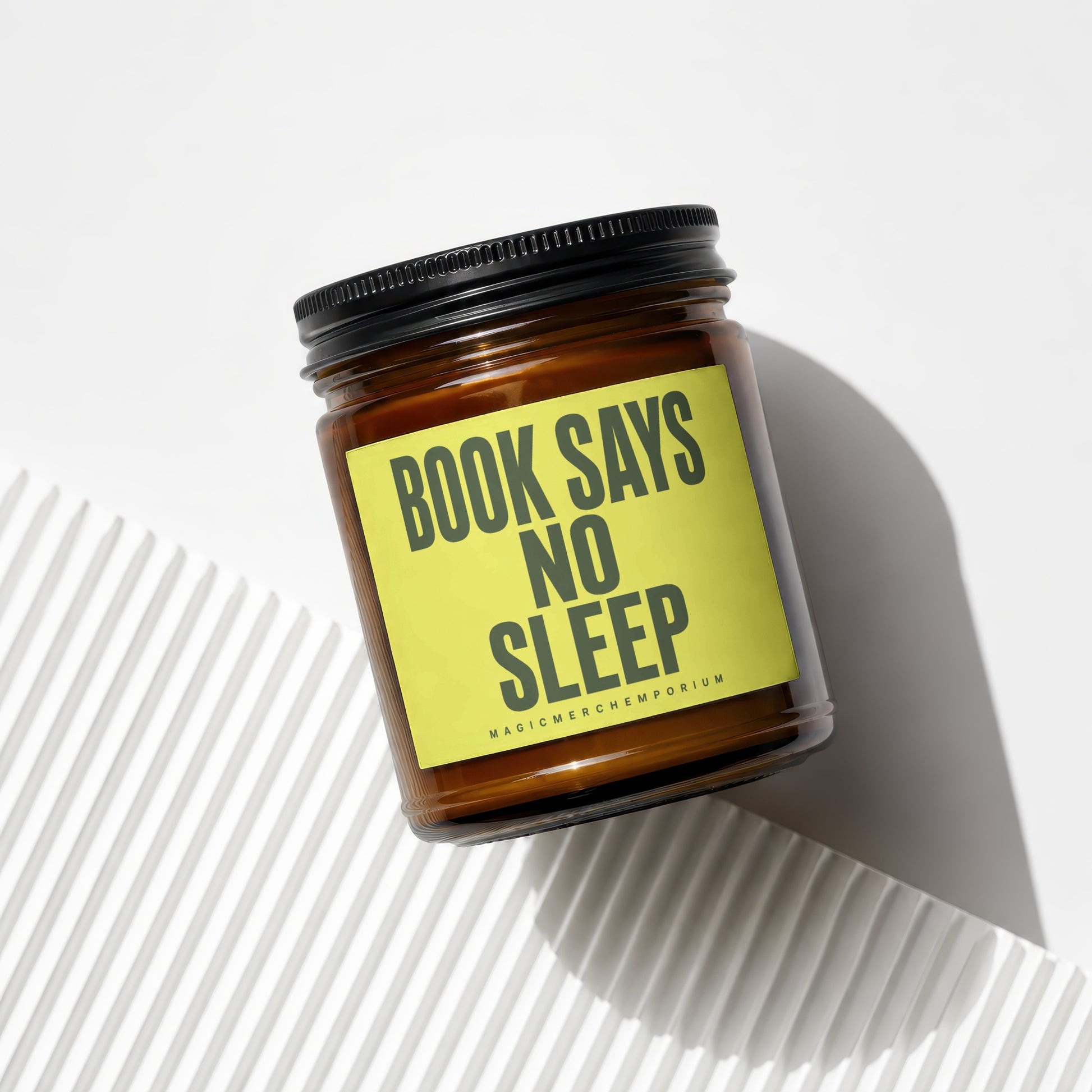 Amber glass candle with yellow label reading "BOOK SAYS NO SLEEP MAGICMERCHEMPORIUM".