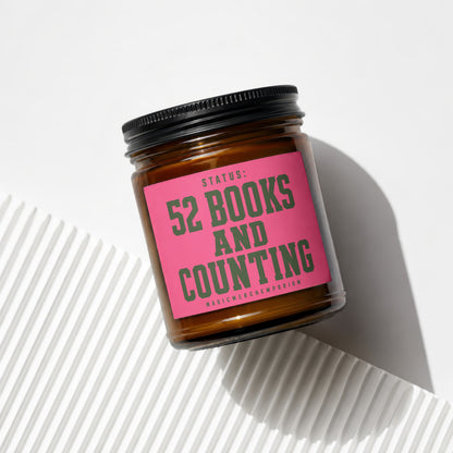 Glass jar candle with pink label reading "Status: 52 Books and Counting".