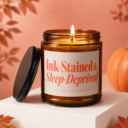 Amber jar candle with lit wick, inscribed "Ink-Stained & Sleep-Deprived".