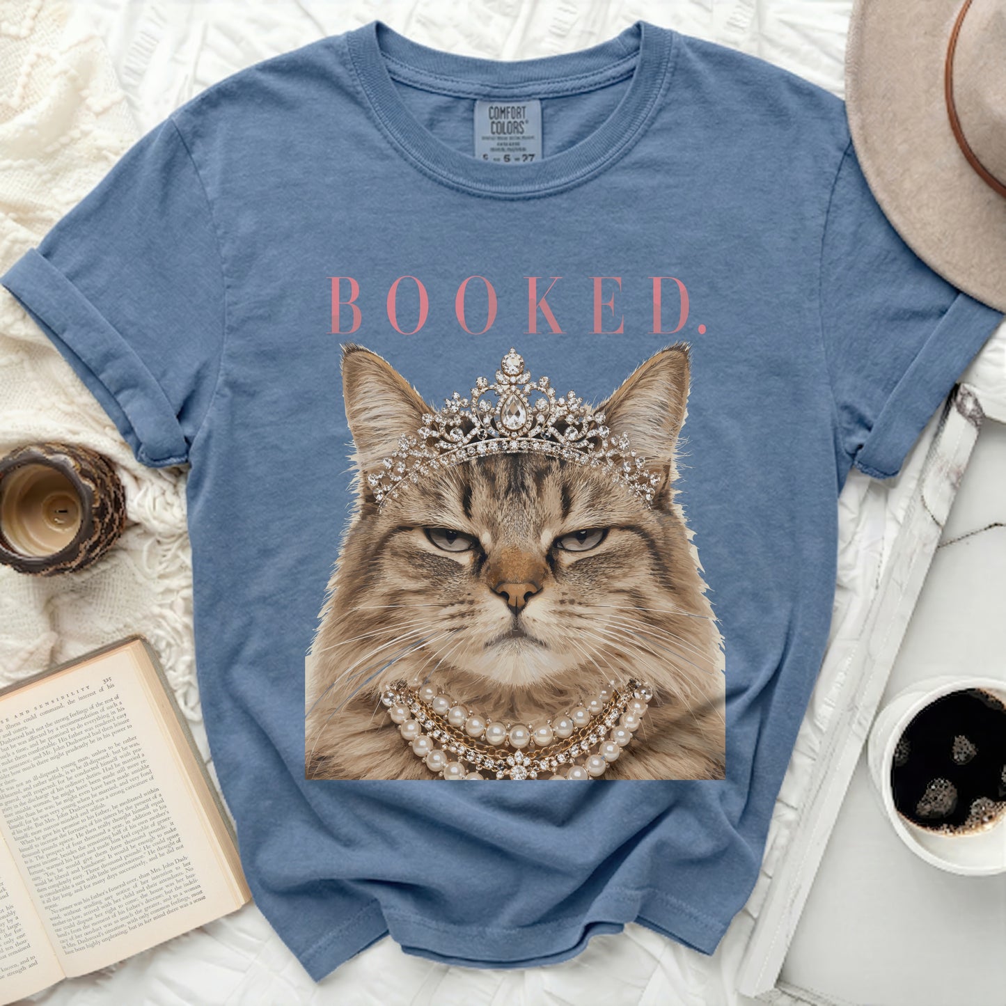 Fuzzy cat wearing a crown and pearl necklace with "BOOKED." text.