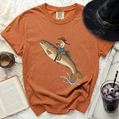 Orange t-shirt with illustration of a woman riding a trout and reading a book.