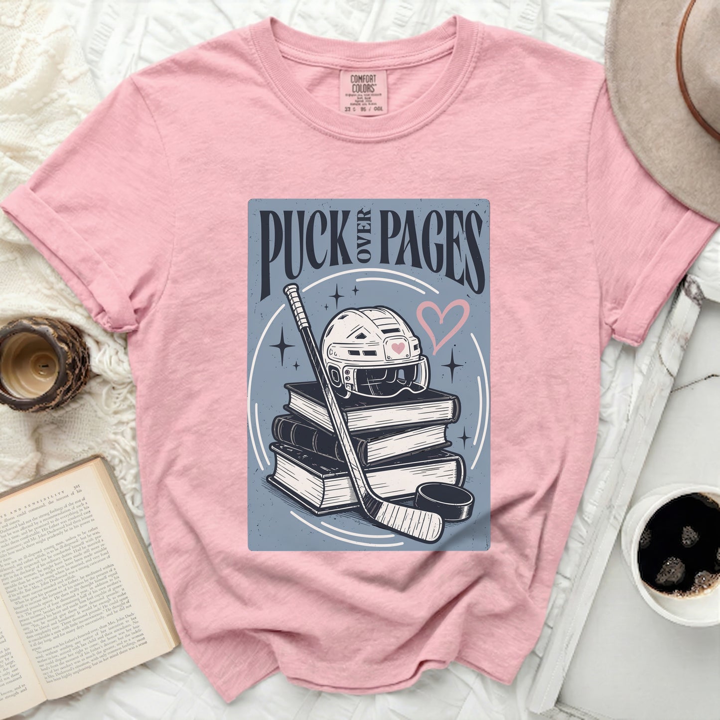 Pink t-shirt with "Puck Over Pages" graphic of hockey gear and books.