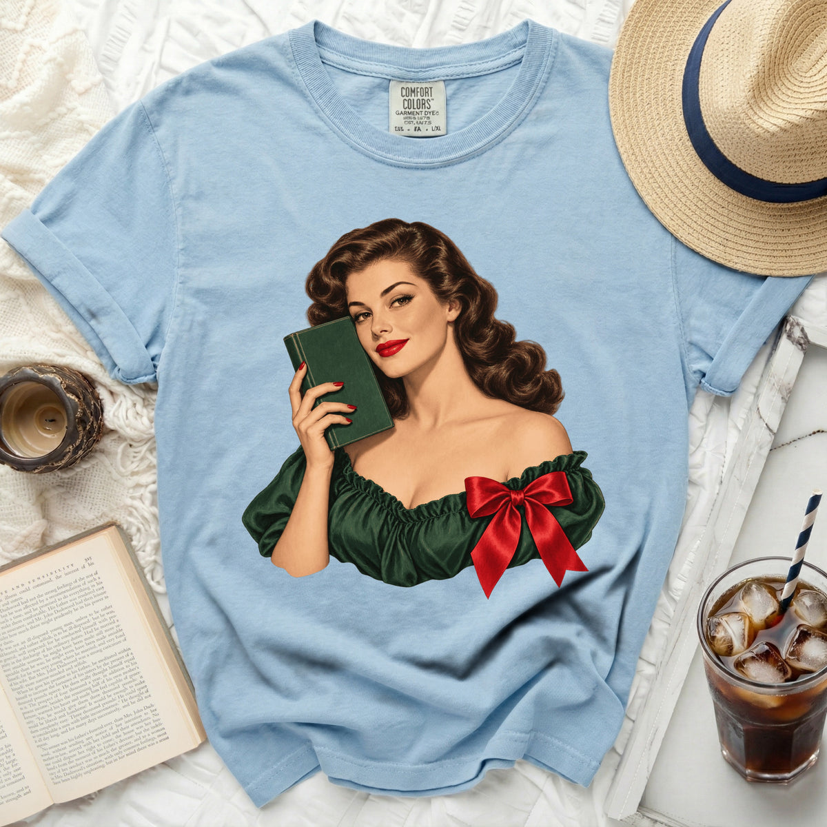 Light blue t-shirt with vintage illustration of woman holding green book and red bow.