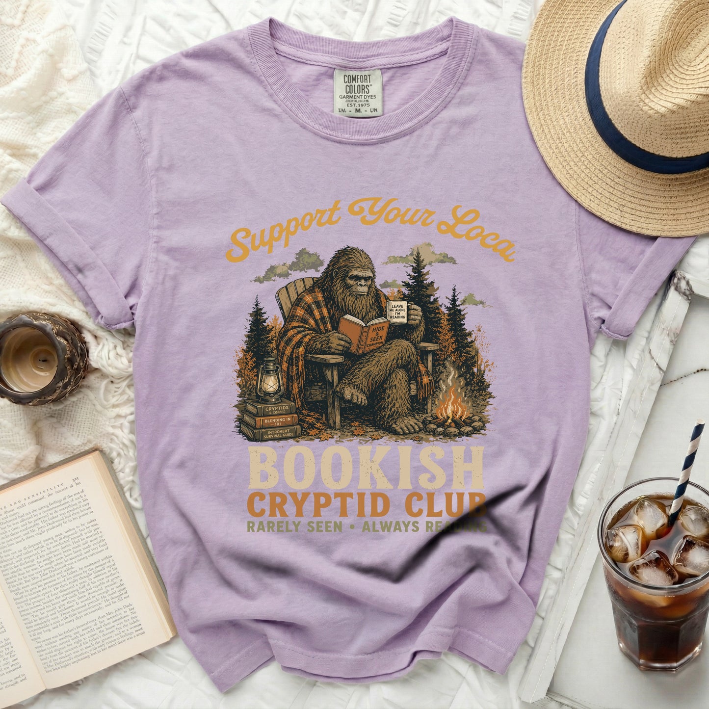 Purple t-shirt with Bigfoot reading and the text "Bookish Cryptid Club".