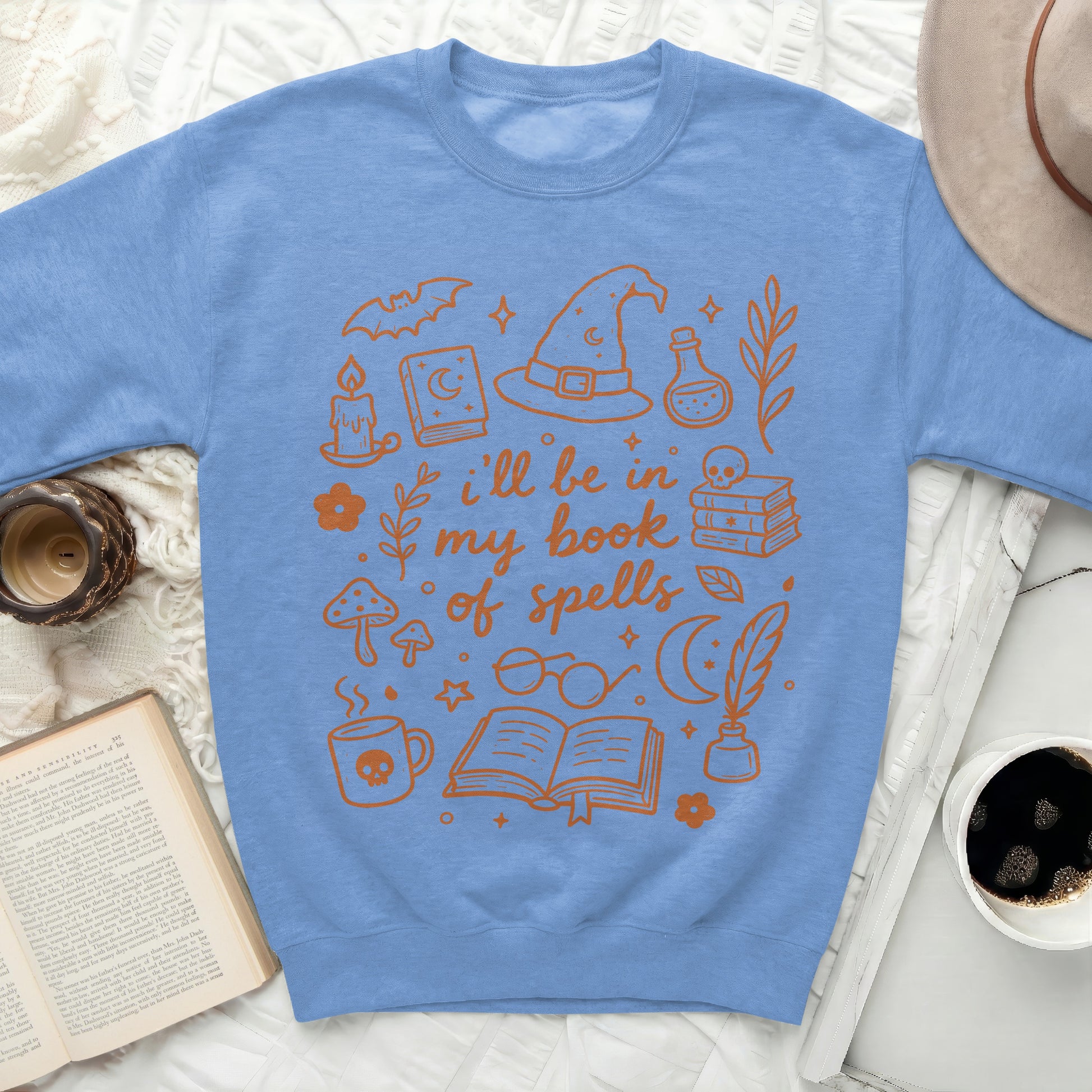 Blue sweatshirt with orange Halloween-themed illustrations and text "i'll be in my book of spells".