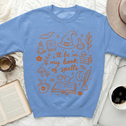 Blue sweatshirt with orange Halloween-themed illustrations and text "i'll be in my book of spells".