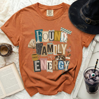 Orange t-shirt with "FOUND FAMILY ENERGY" text graphic, cat, and book elements.