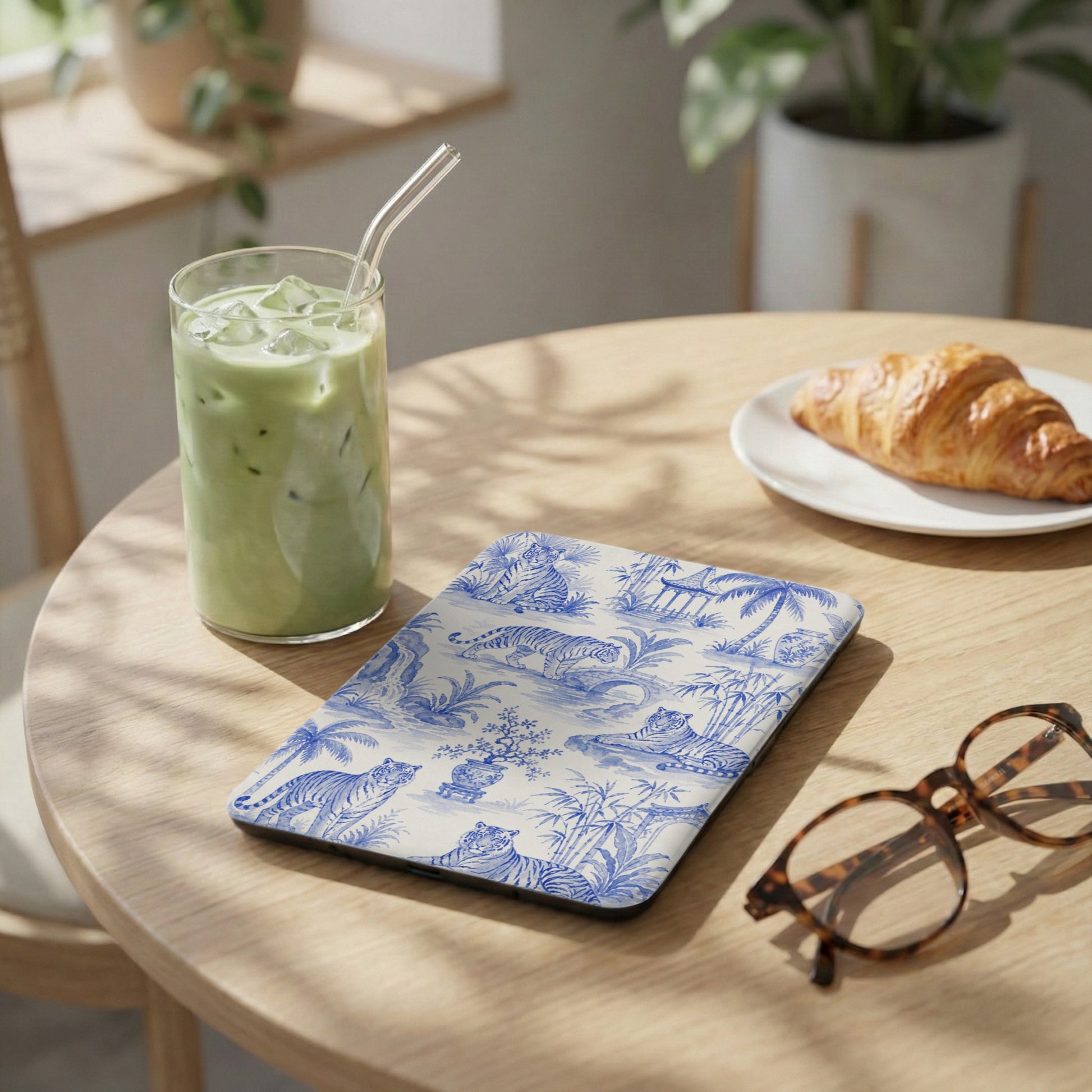 Tablet with blue and white tiger toile pattern, next to a matcha drink and croissant.