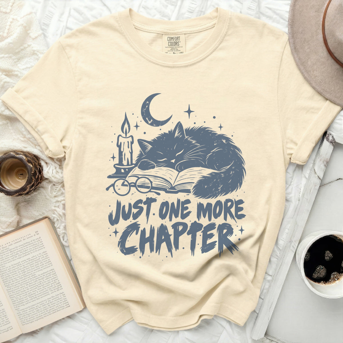 Cream t-shirt with "Just One More Chapter" and sleeping cat graphic.