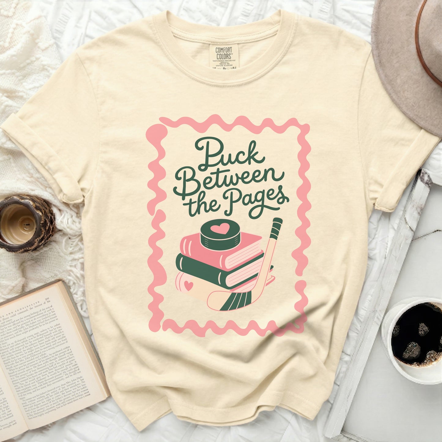 Cream t-shirt with "Puck Between the Pages" text and hockey puck.