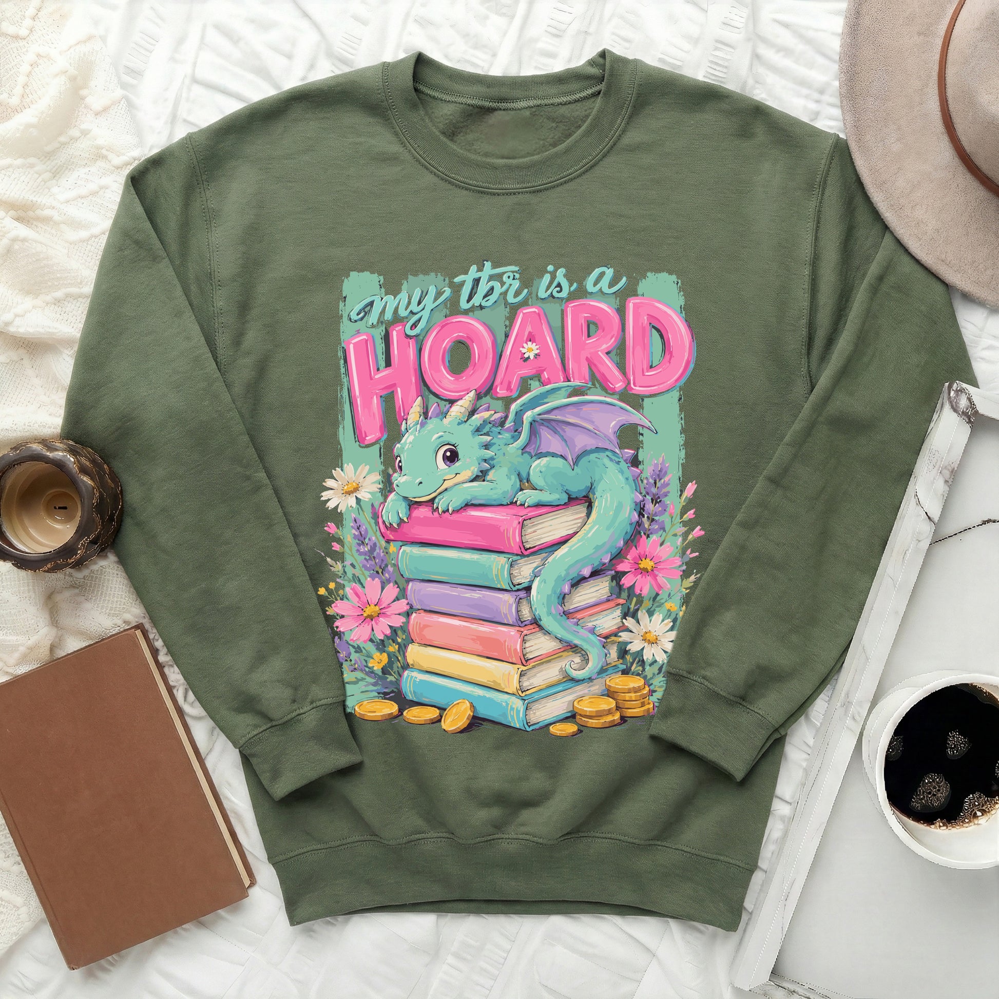 Green sweatshirt with a cartoon dragon on a stack of books and text "my tbr is a hoard".