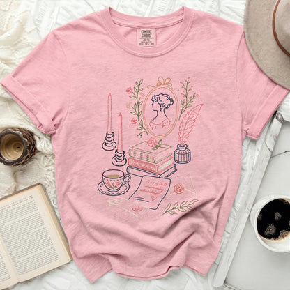 Pink t-shirt with embroidered literary scene including portrait, books, tea cup, quill, and text.