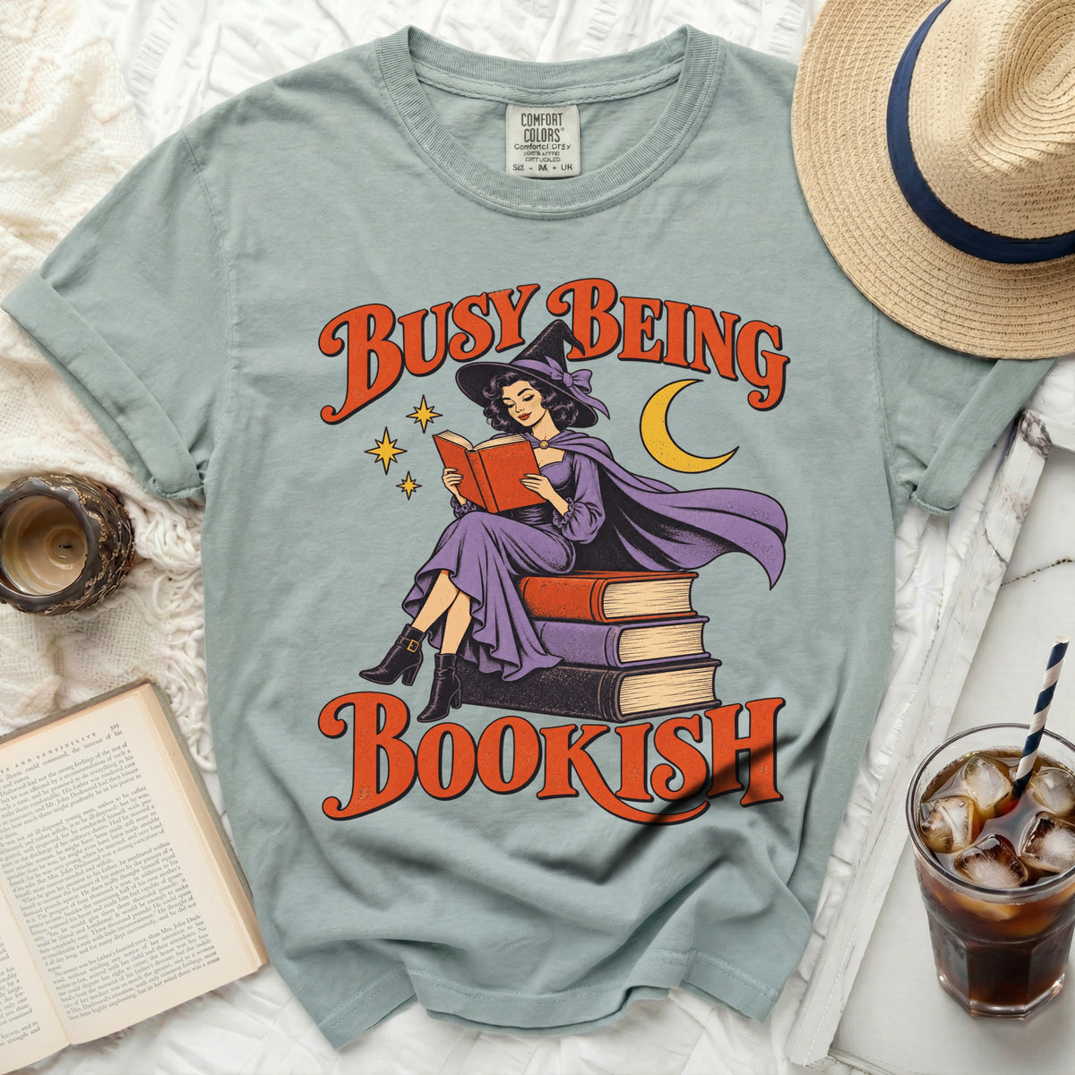 Witch reading book on stack of books with text "BUSY BEING BOOKISH".