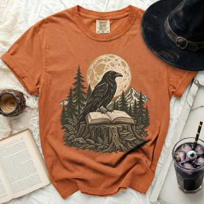 Orange t-shirt with a raven on a book on a tree stump, full moon, and trees.