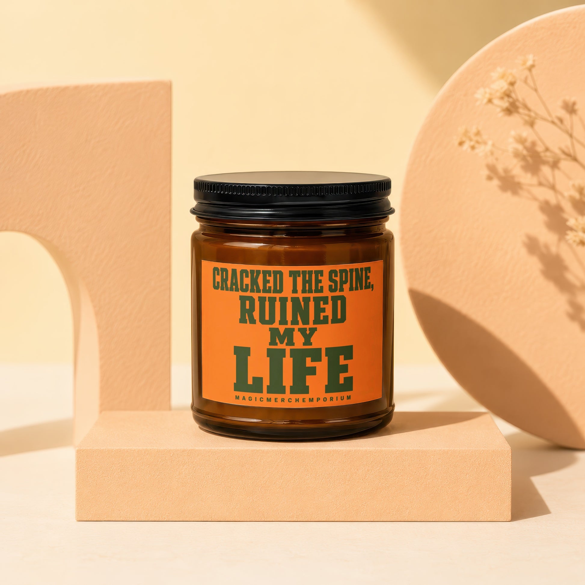Brown glass candle with orange label saying "CRACKED THE SPINE, RUINED MY LIFE".