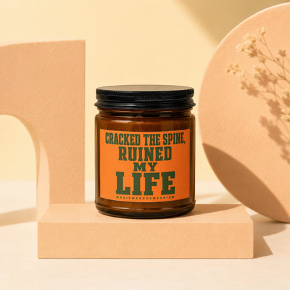 Brown glass candle with orange label saying "CRACKED THE SPINE, RUINED MY LIFE".