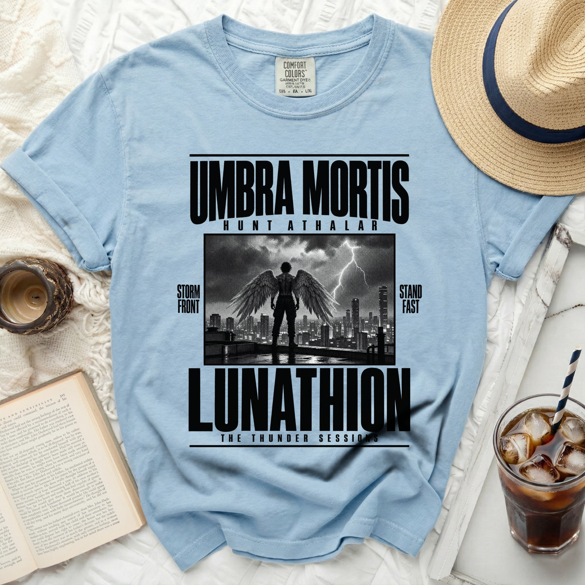 Light blue t-shirt with "UMBRA MORTIS" and "LUNATHION" text, winged figure, city, and lightning.