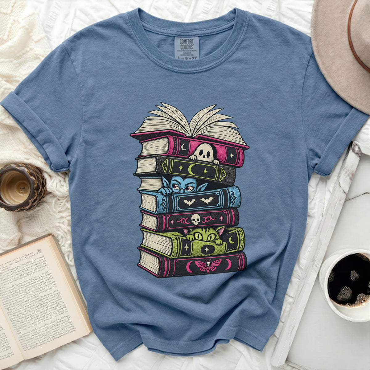 T-shirt with a stack of Halloween-themed books and cute characters.