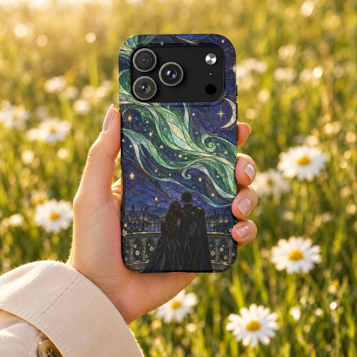 A hand holds a smartphone with a stained-glass style case depicting a couple gazing at a starry night sky above a city.