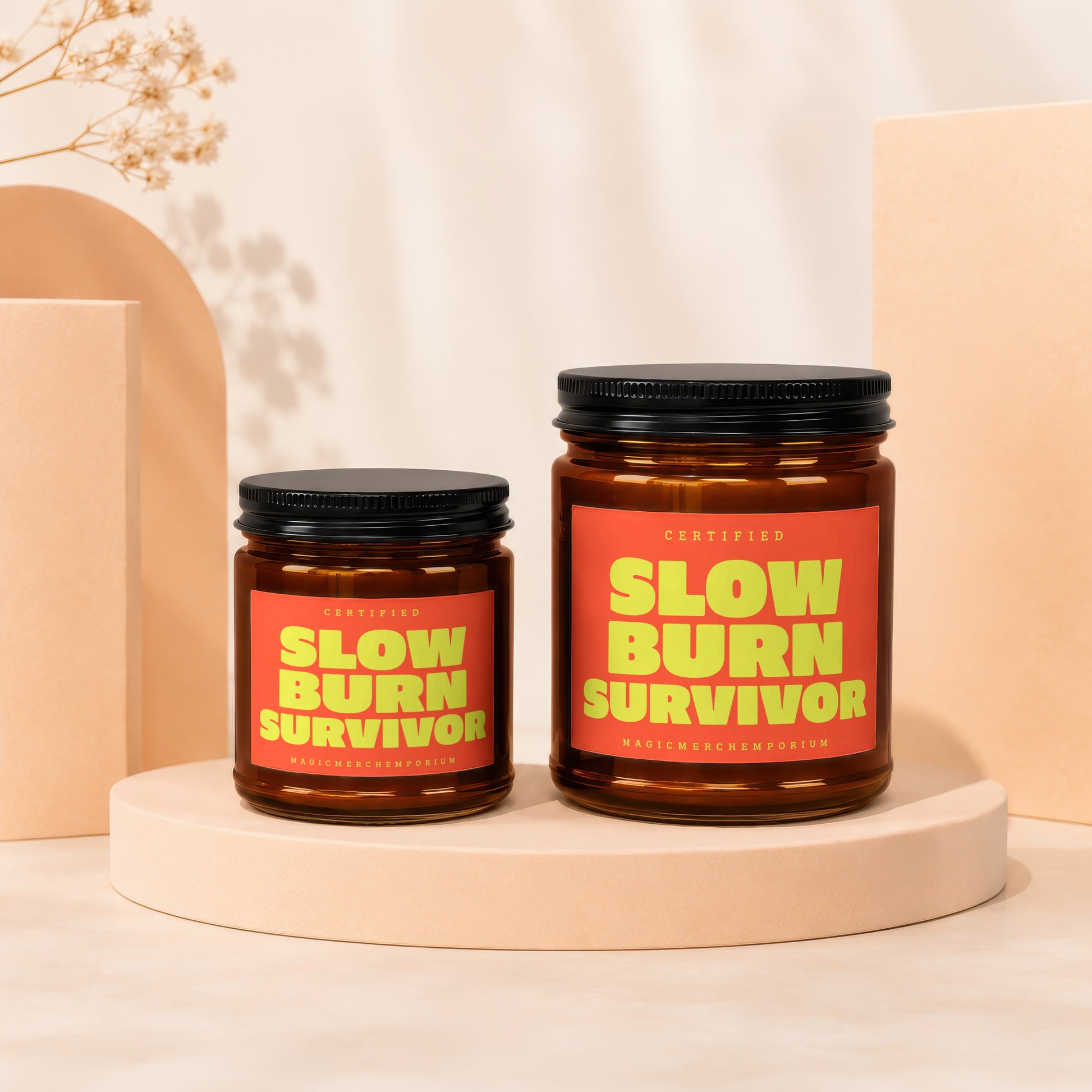 Two amber glass candles with black lids, featuring "Certified Slow Burn Survivor" on orange labels.