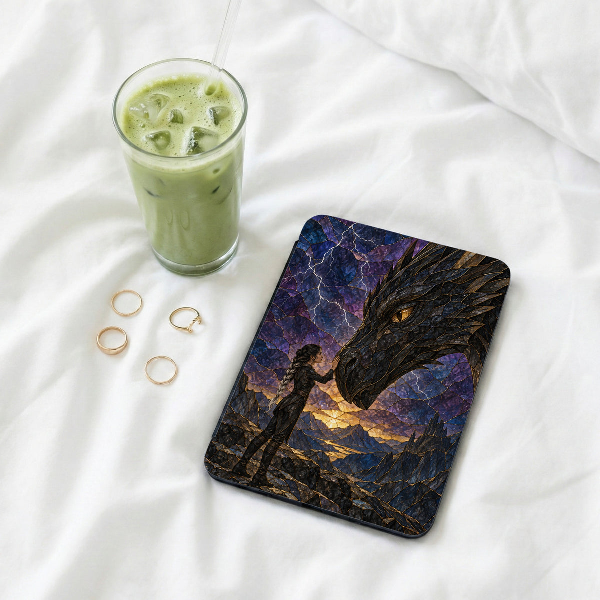Tablet case with dragon and woman design next to a green drink and rings.