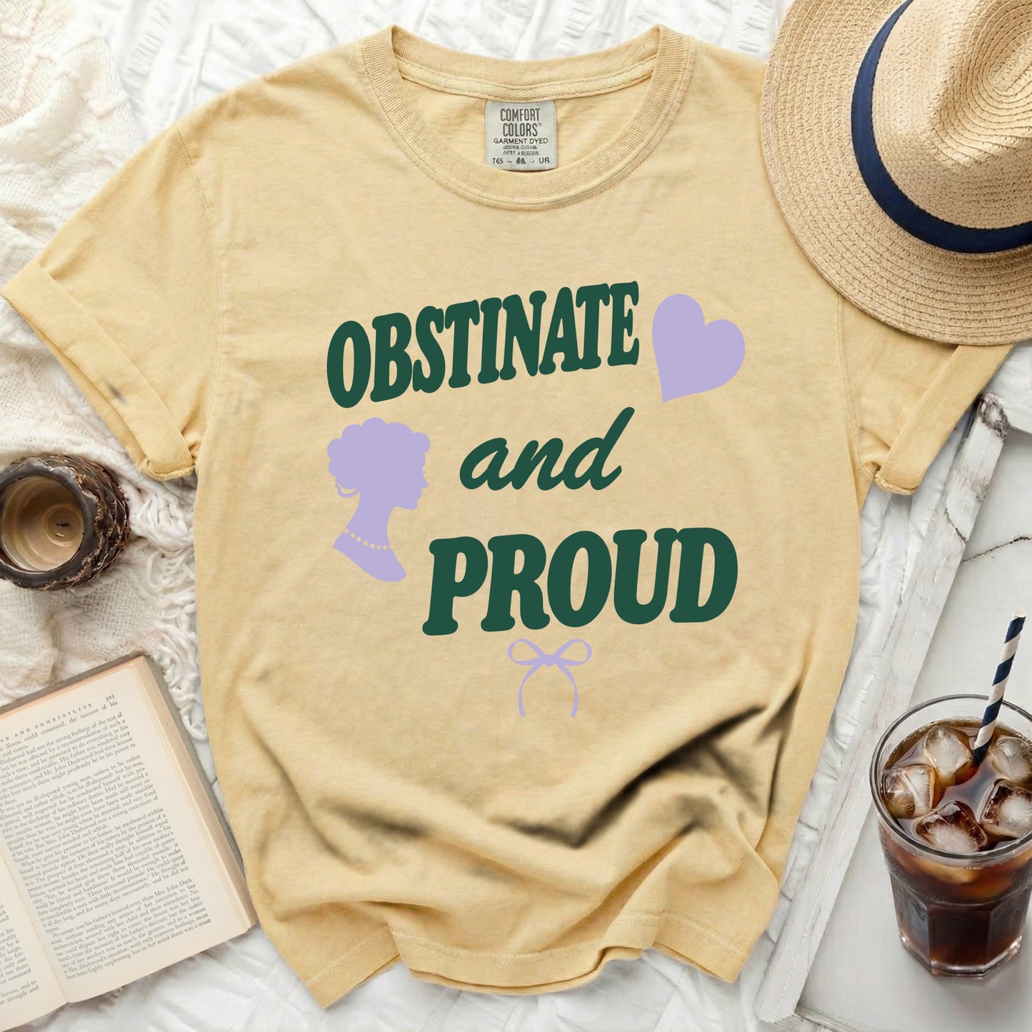 Yellow shirt with green text "OBSTINATE and PROUD", purple silhouette, and bow.