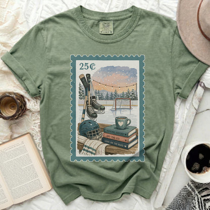 Green t-shirt with postage stamp graphic of hockey scene, books, and coffee.