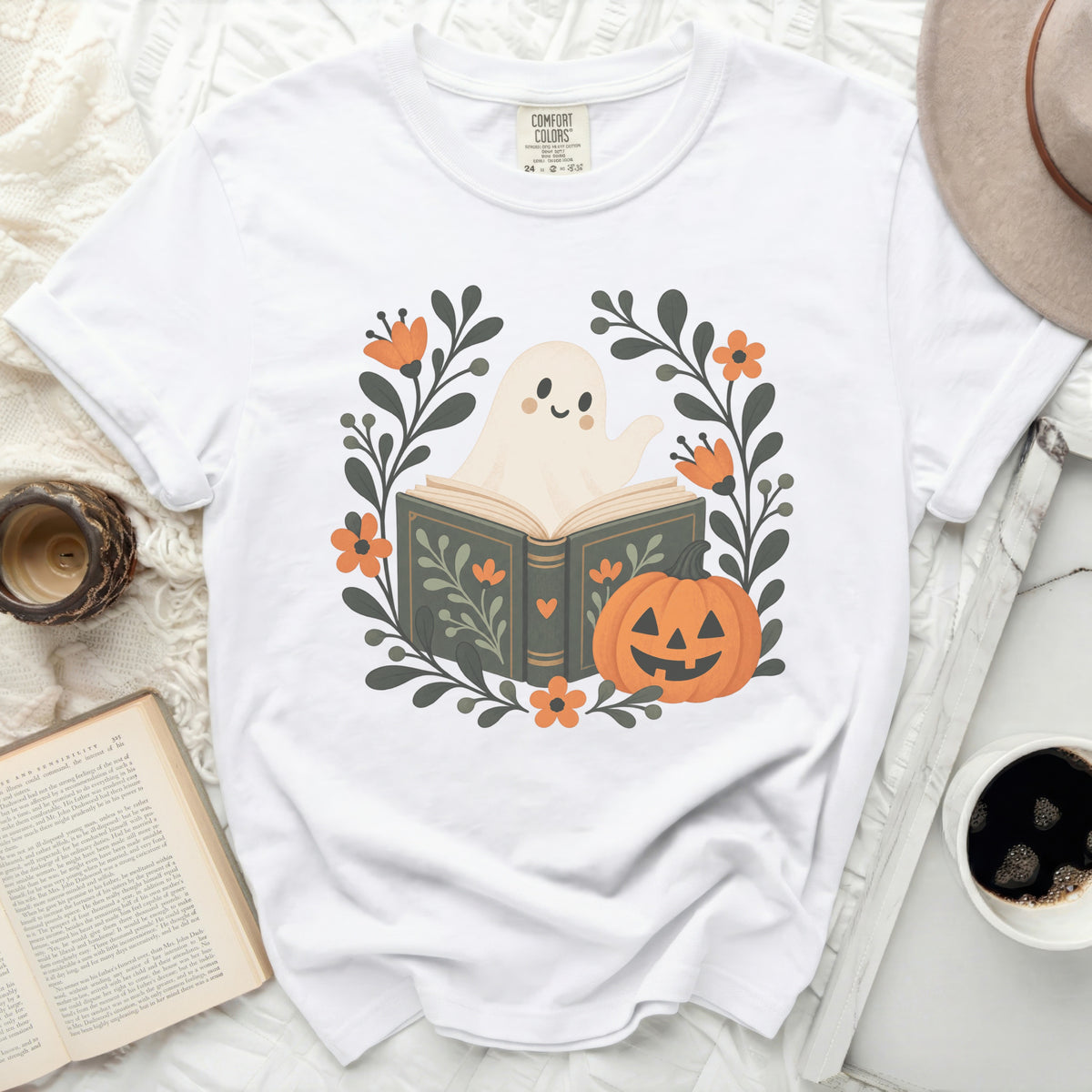 White t-shirt with a graphic of a ghost reading a book surrounded by flowers and a pumpkin.
