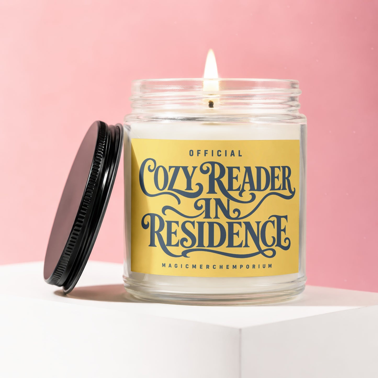 Lit jar candle with yellow label reading "OFFICIAL COZY READER IN RESIDENCE"