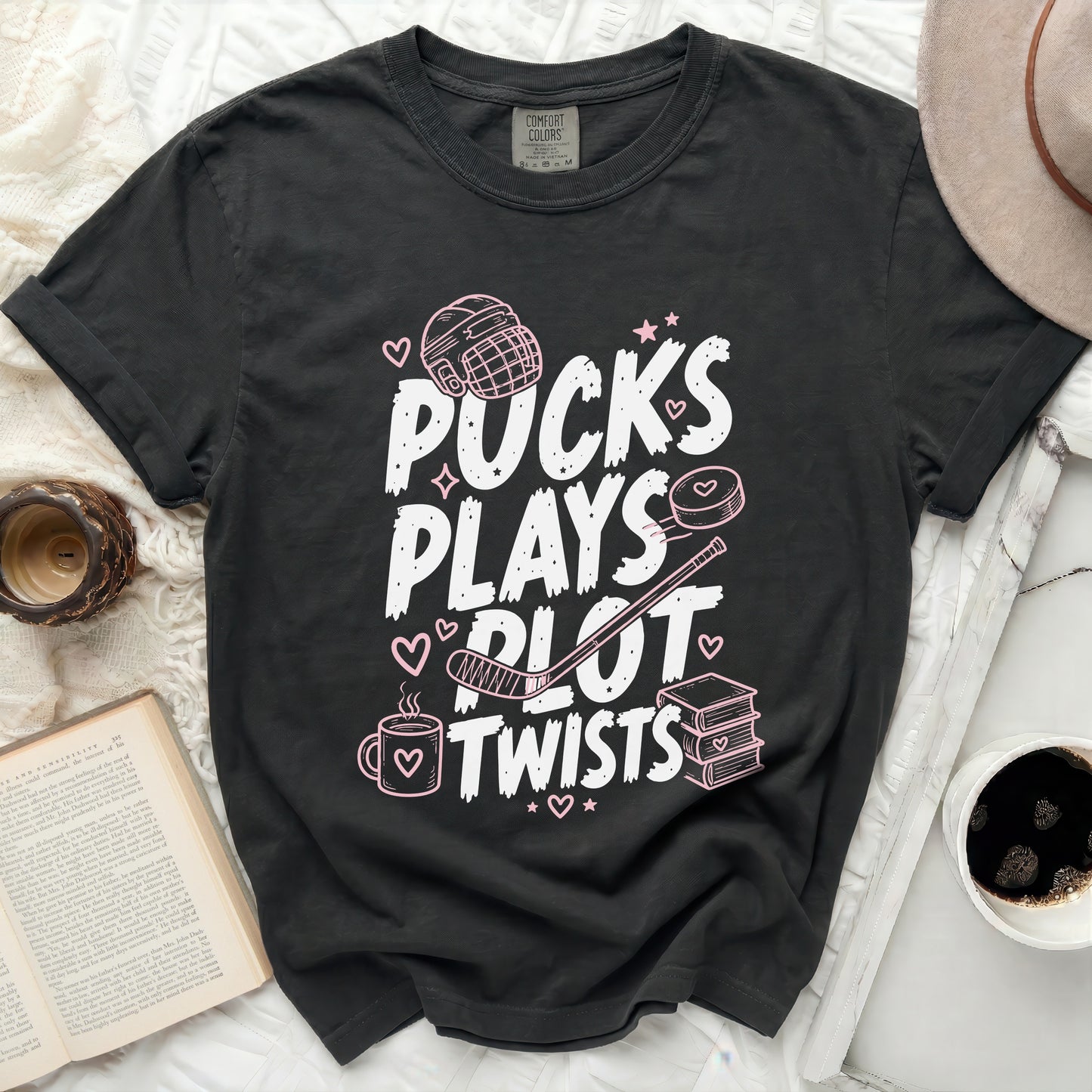 Black t-shirt with "Pucks Plays Plot Twists" in pink lettering and hockey graphics.