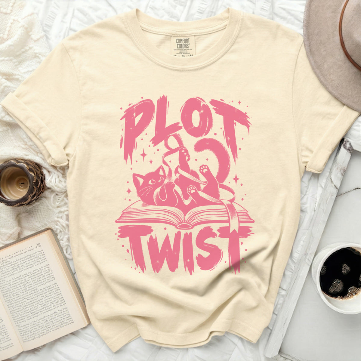 Cream t-shirt with pink "Plot Twist" graphic featuring a cat tangled in ribbon on an open book.