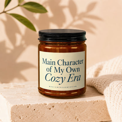 Candle with text "Main Character of My Own Cozy Era" on cream label.