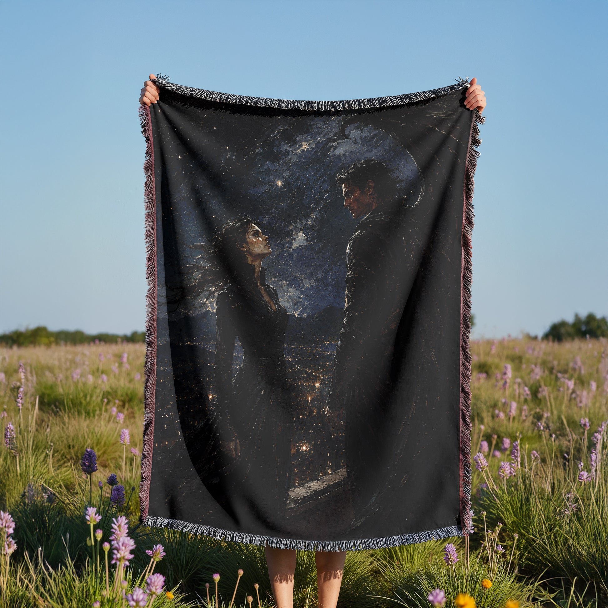 A person is holding a black blanket with a painting of two people on it, standing in a field with purple flowers.