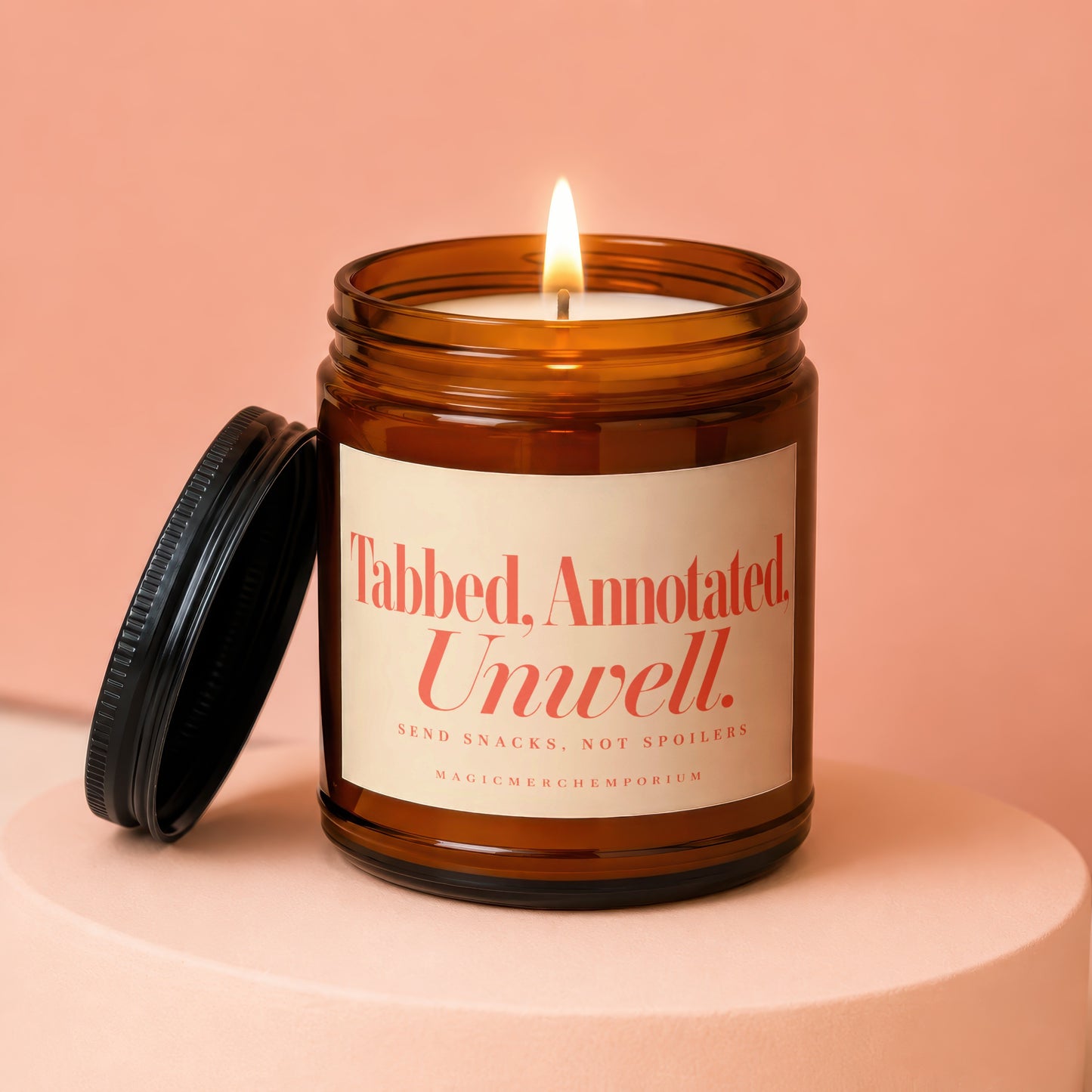 A lit amber jar candle with a black lid rests on a pedestal against a peach background.